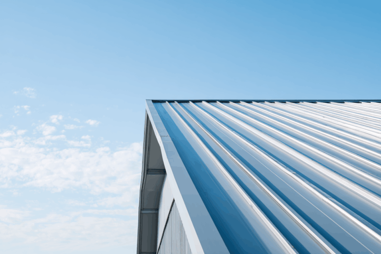 Vue extérieure d’un toit en bac acier moderne avec reflets du ciel, photographié en légère contre-plongée sous une lumière naturelle.
